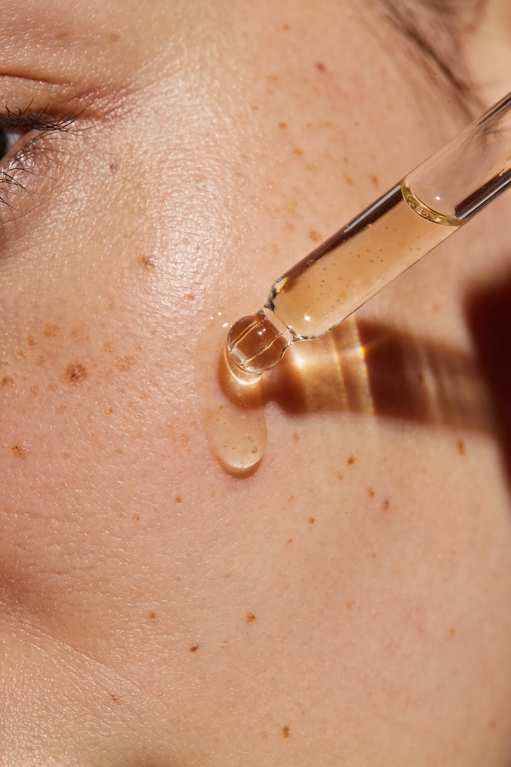 Golden facial oil dropping from a glass pipette onto freckled skin — Brand Design by Parallel Creative Agency — Derma, beauty and cosmetics