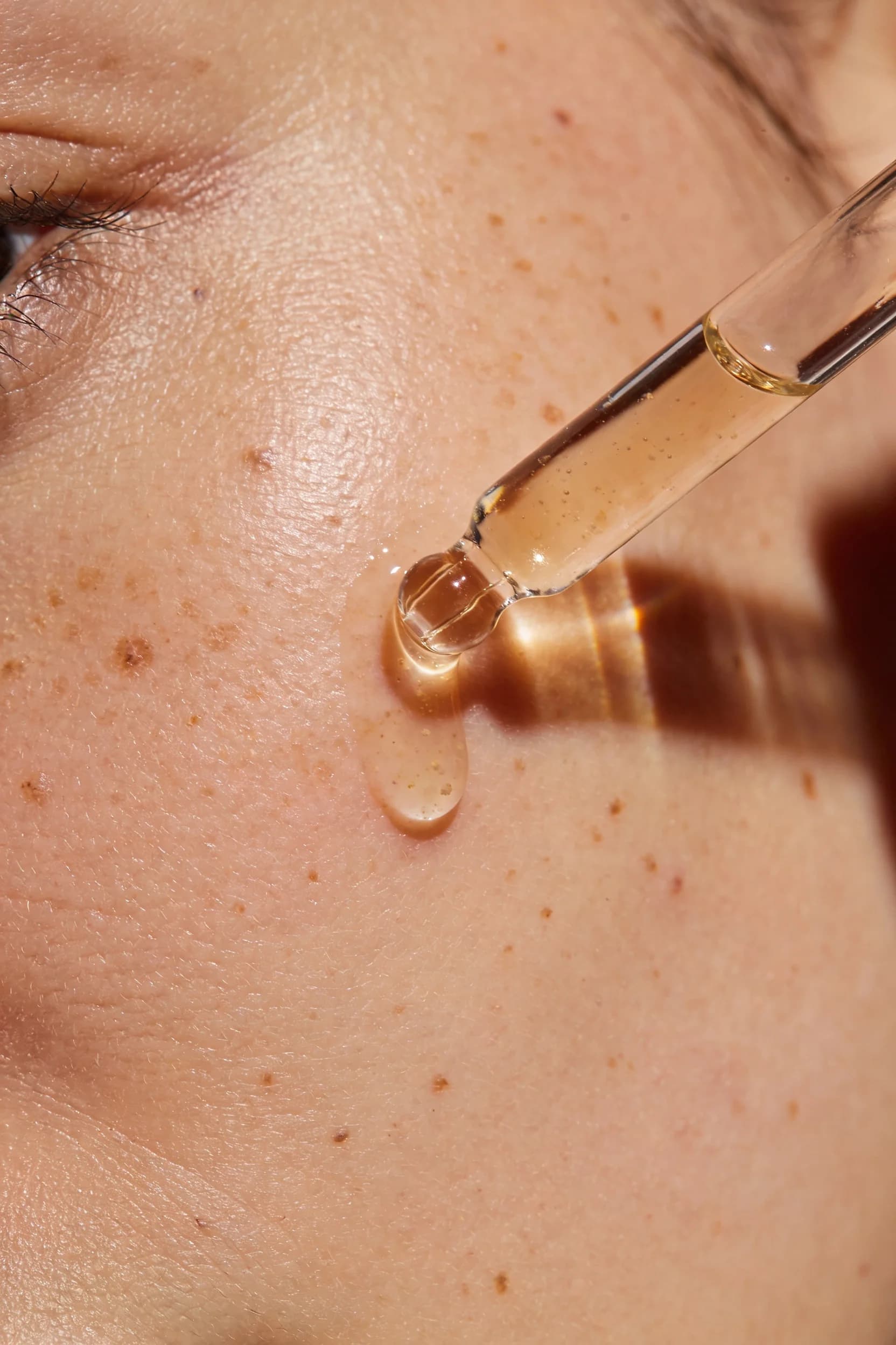 Golden facial oil dropping from a glass pipette onto freckled skin — Brand Design by Parallel Creative Agency — Derma, beauty and cosmetics