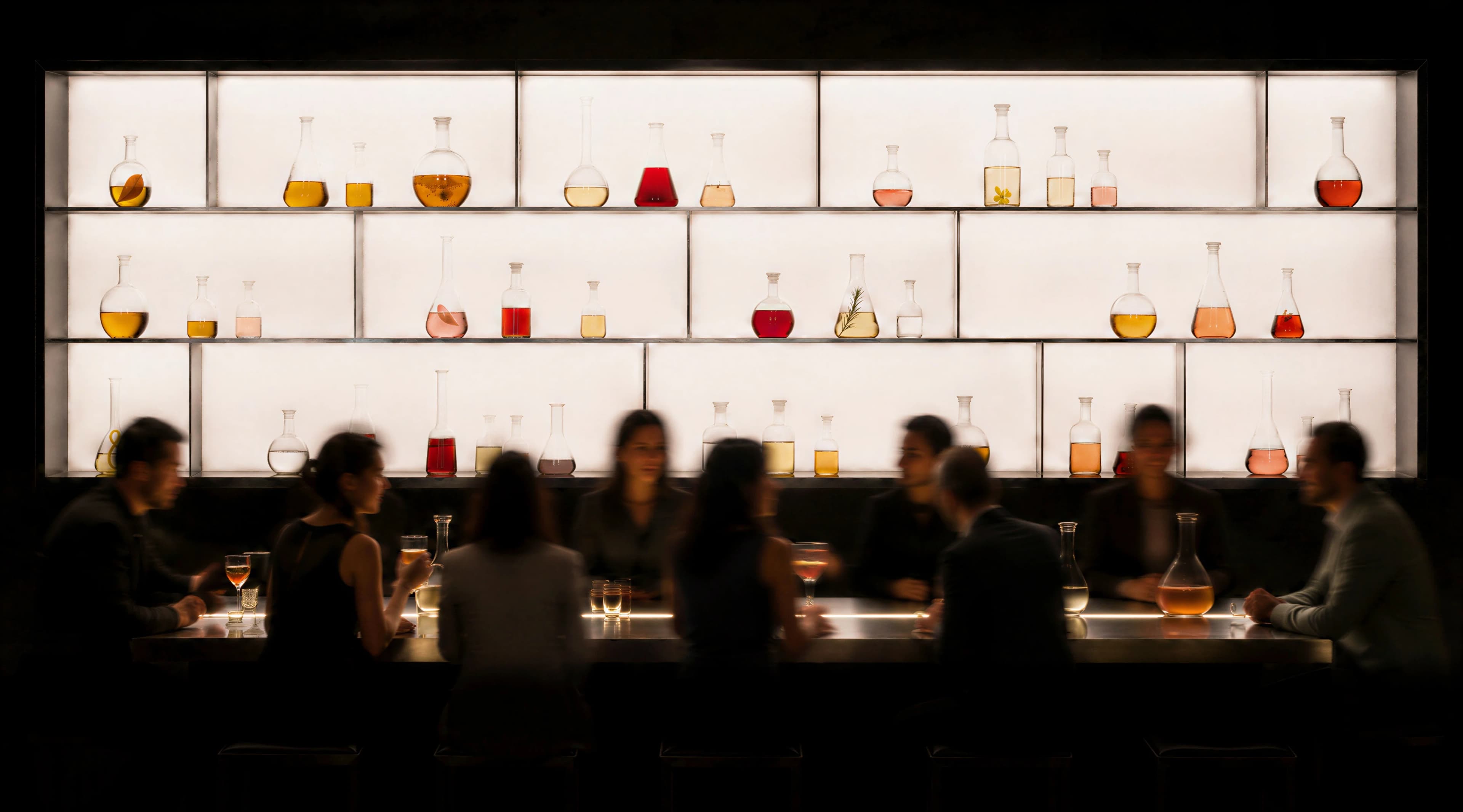 Guests socialising at a dark cocktail bar in front of an illuminated ingredient library — Experience Design by Parallel Creative Agency — Elixir, hospitality