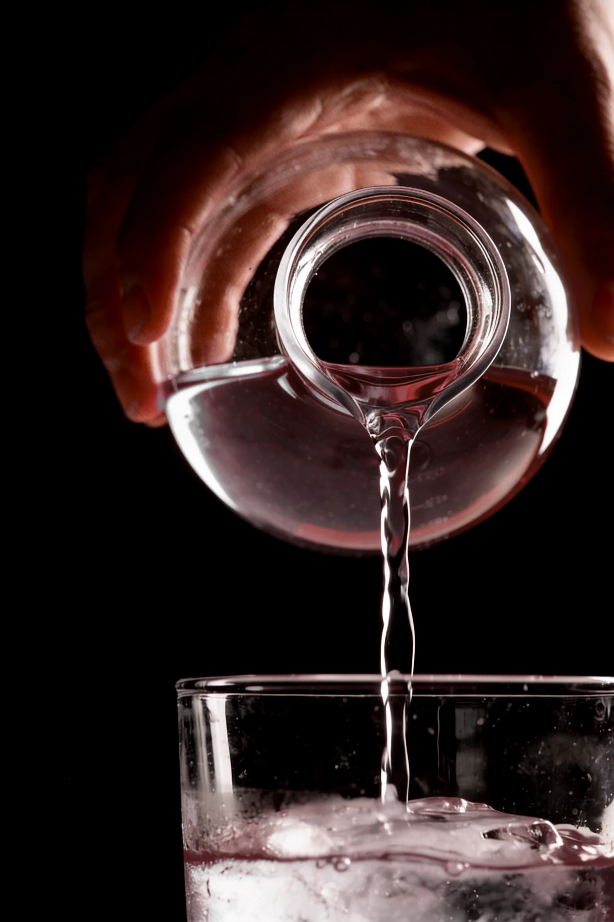 Clear spirit poured from a round laboratory vessel into a glass over ice — Product Design by Parallel Creative Agency — Elixir, drinks