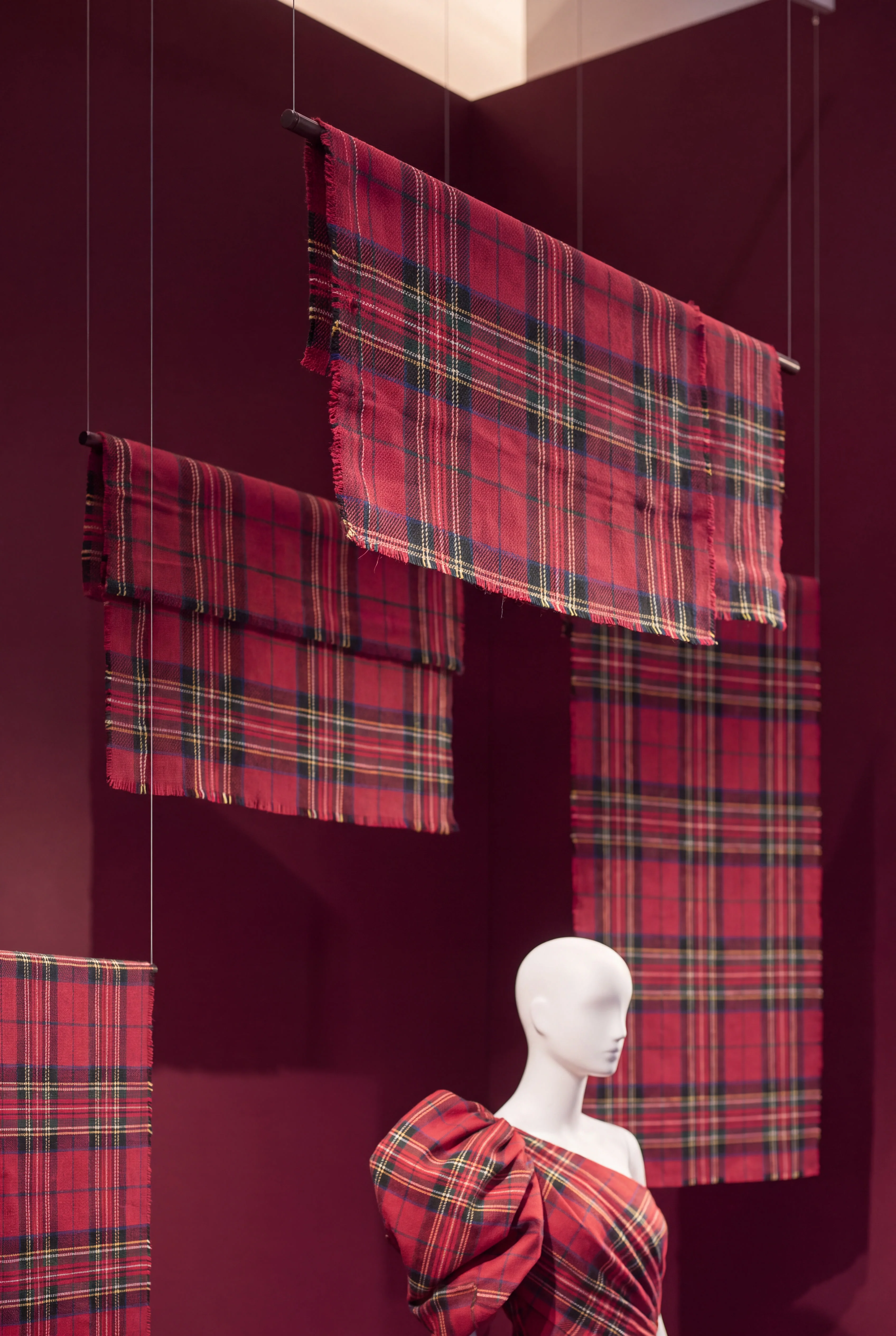 Red tartan fashion garment displayed beneath hanging woven tartan panels — Window Concept by Parallel Creative Agency — Loom, fashion