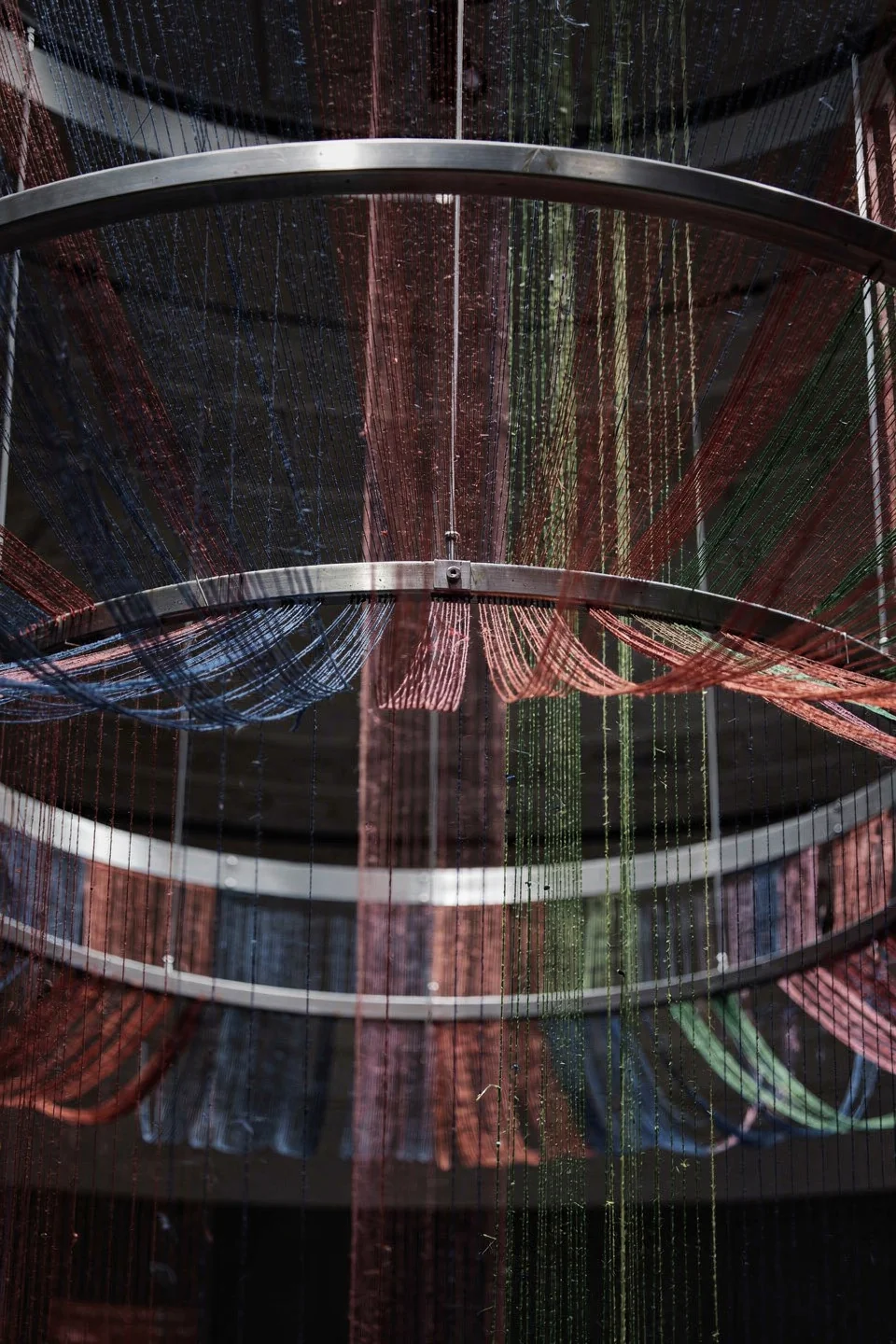 Coloured threads cascading through circular metal frames above the exhibition — Spatial Design by Parallel Creative Agency — Loom, culture