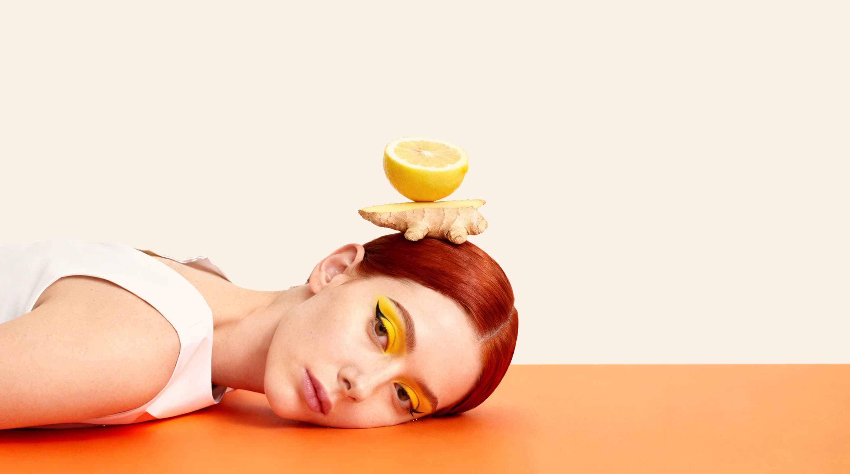 Model lying against an orange backdrop with lemon and ginger balanced above her head — Campaign Direction by Parallel Creative Agency — Love Ginger, drinks