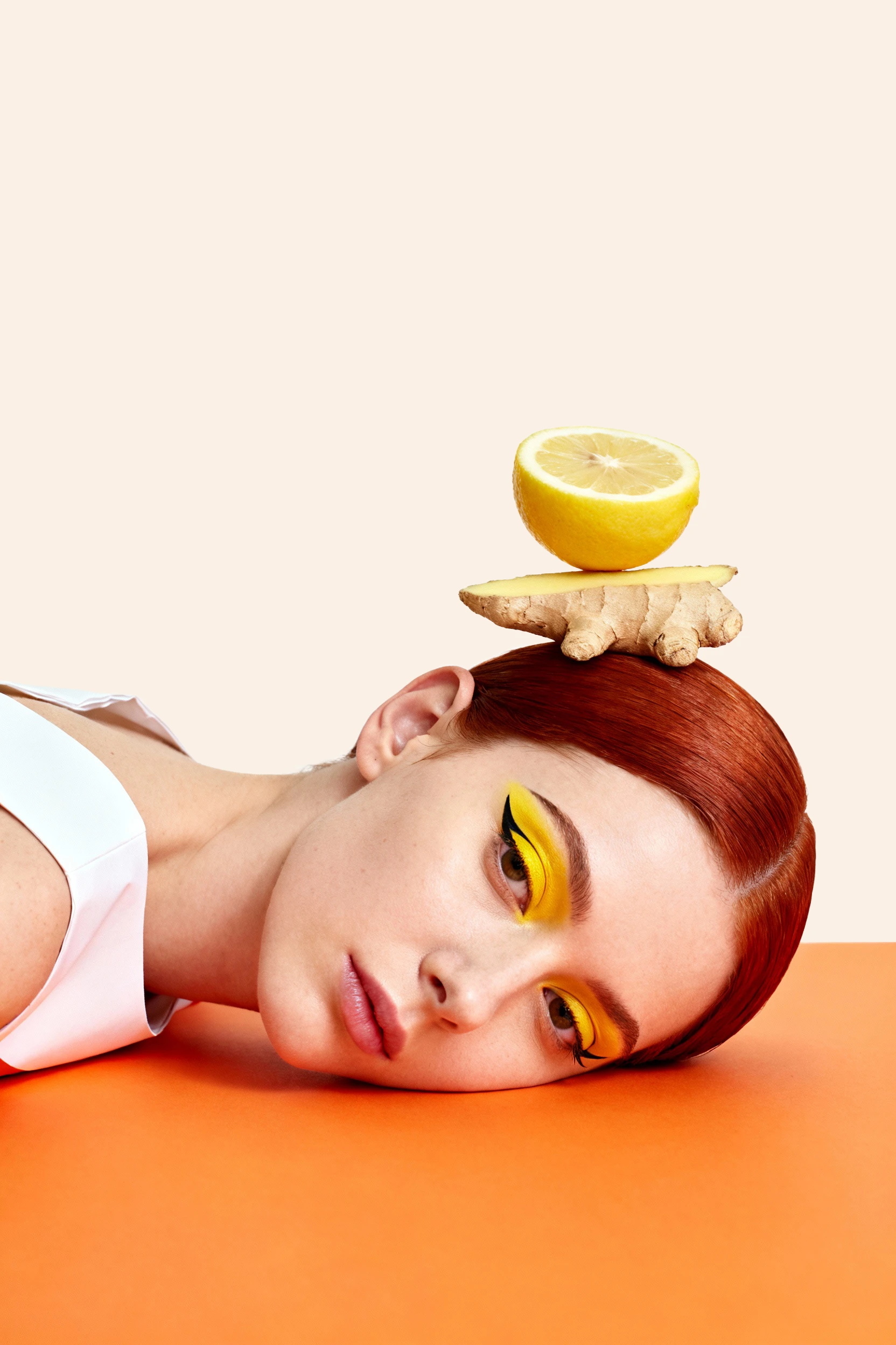 Model resting on an orange surface with stacked ginger and lemon above her head — Campaign Direction by Parallel Creative Agency — Love Ginger, drinks