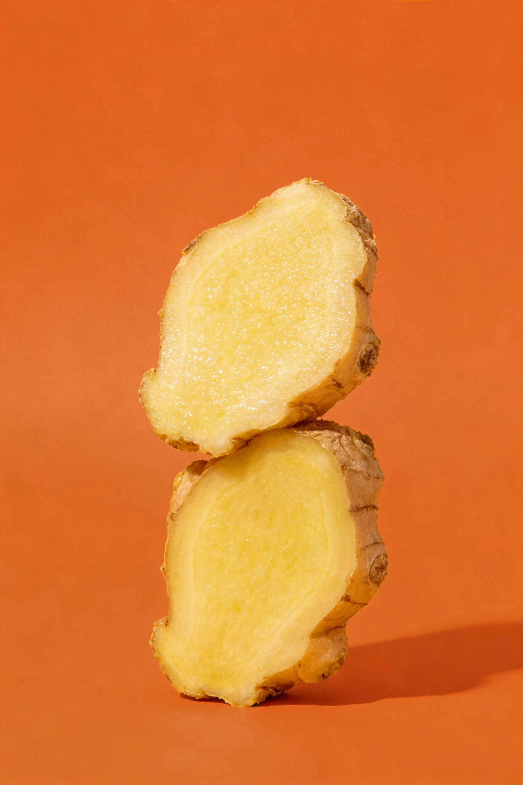 Two ginger root slices balanced vertically against an orange background — Product Design by Parallel Creative Agency — Love Ginger, drinks