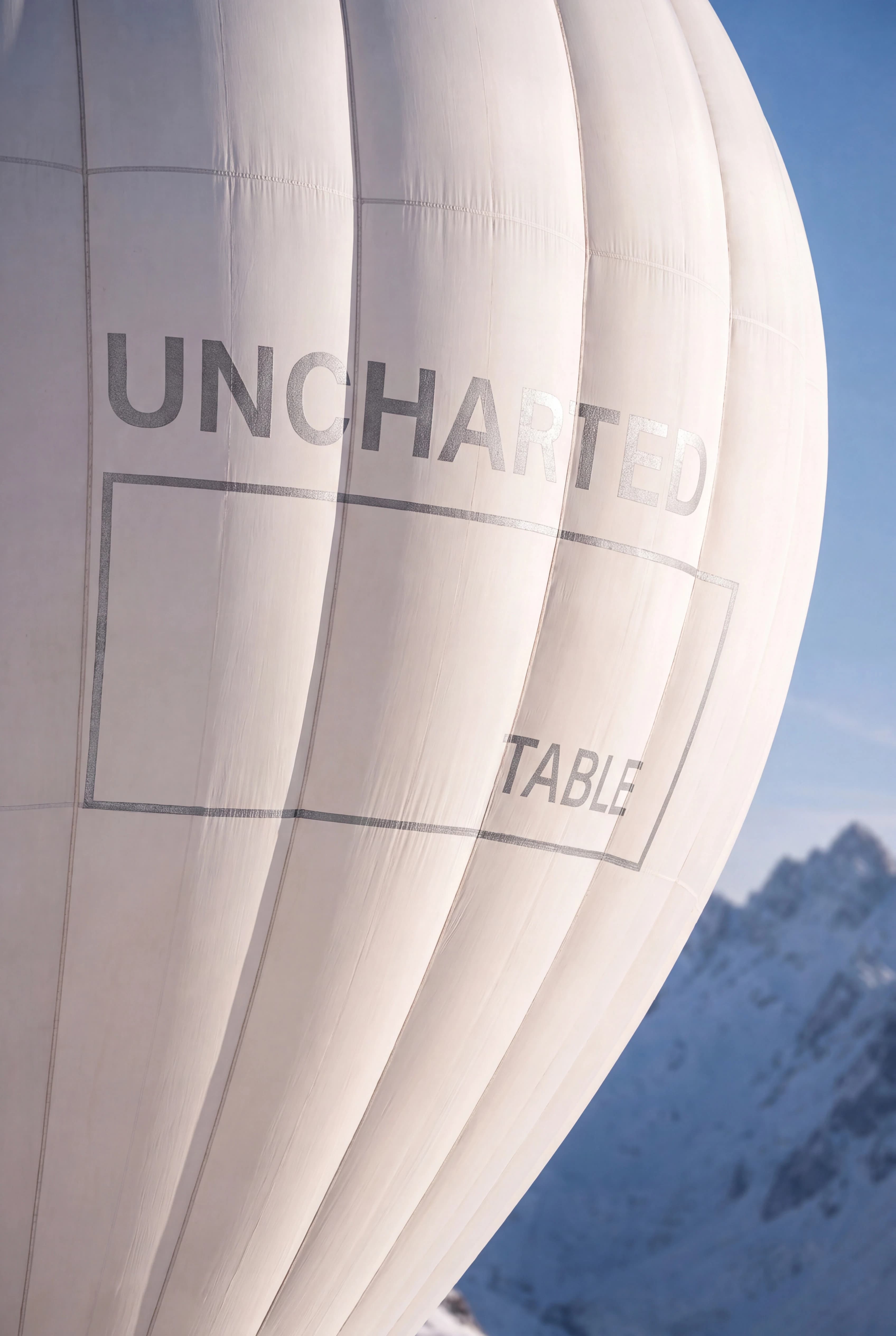 Close-up of Uncharted Table branding on a hot-air balloon above snowy mountains — Brand Design by Parallel Creative Agency — Uncharted Table, hospitality and travel