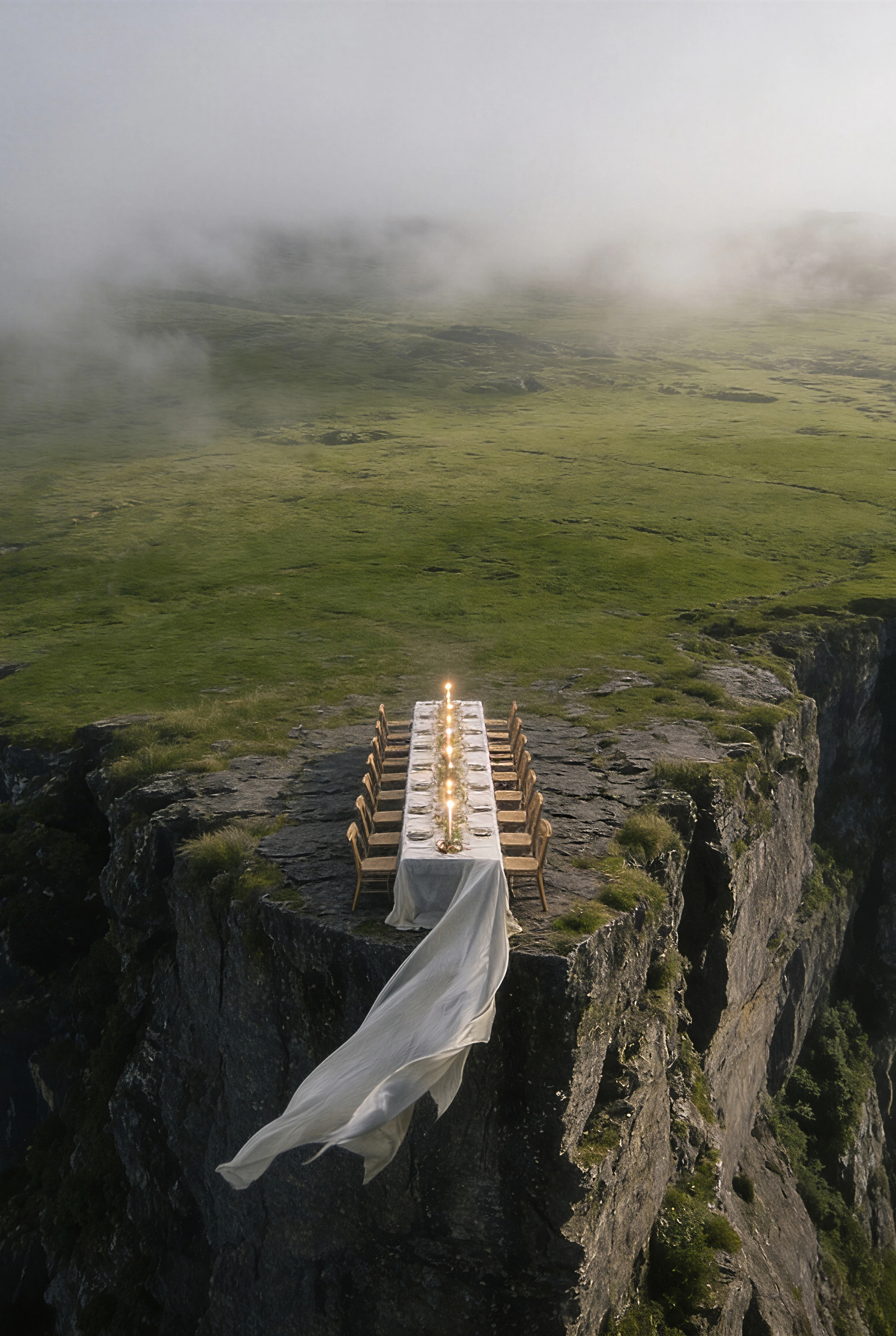 Vertical aerial view of an intimate dining table suspended beyond a grassy sea cliff — Experience Design by Parallel Creative Agency — Uncharted Table, hospitality and travel