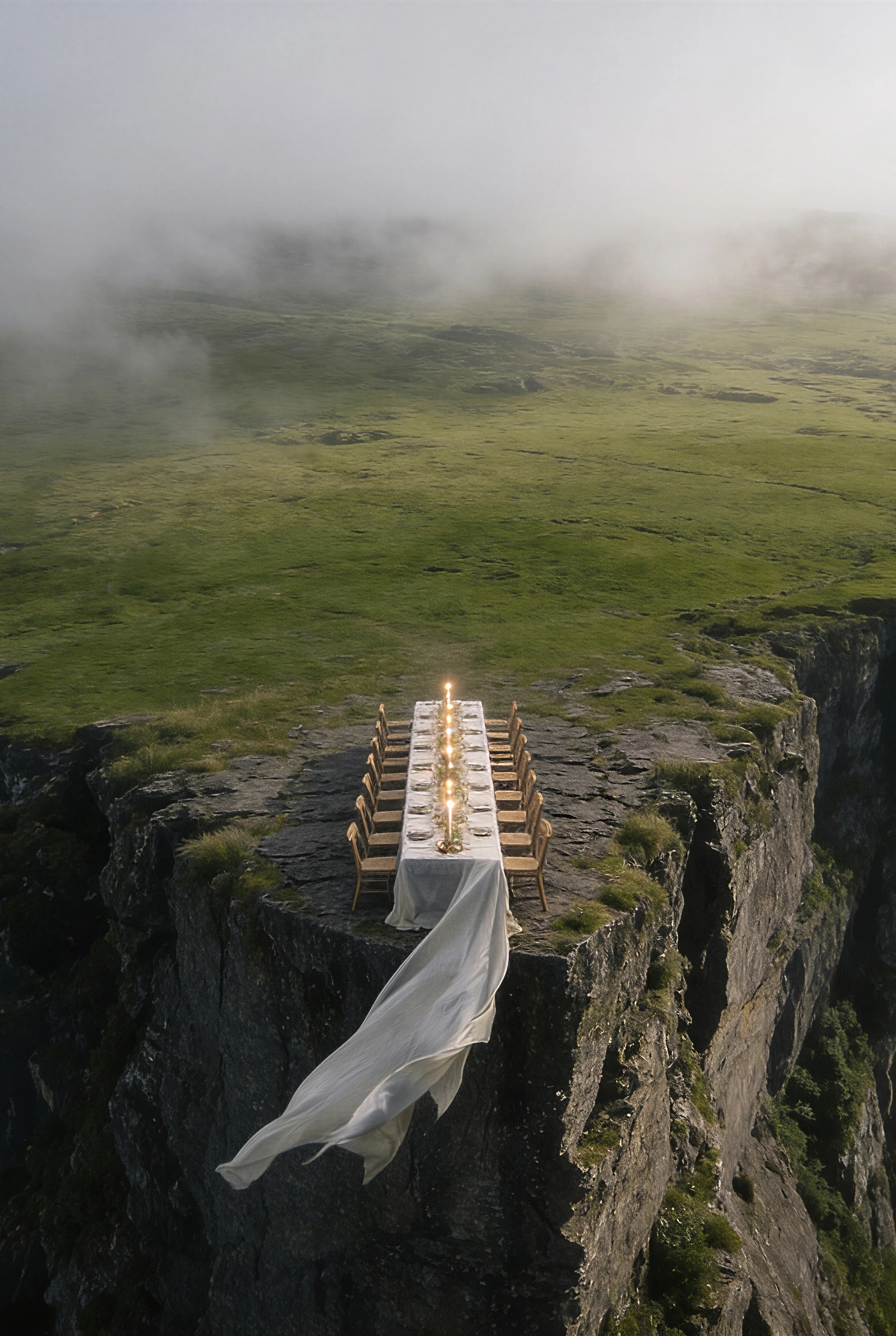 Vertical aerial view of an intimate dining table suspended beyond a grassy sea cliff — Experience Design by Parallel Creative Agency — Uncharted Table, hospitality and travel